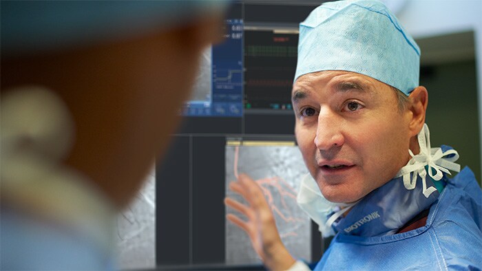 Doctor looks at another doctor right in front of camera while pointing at scan images on a monitor