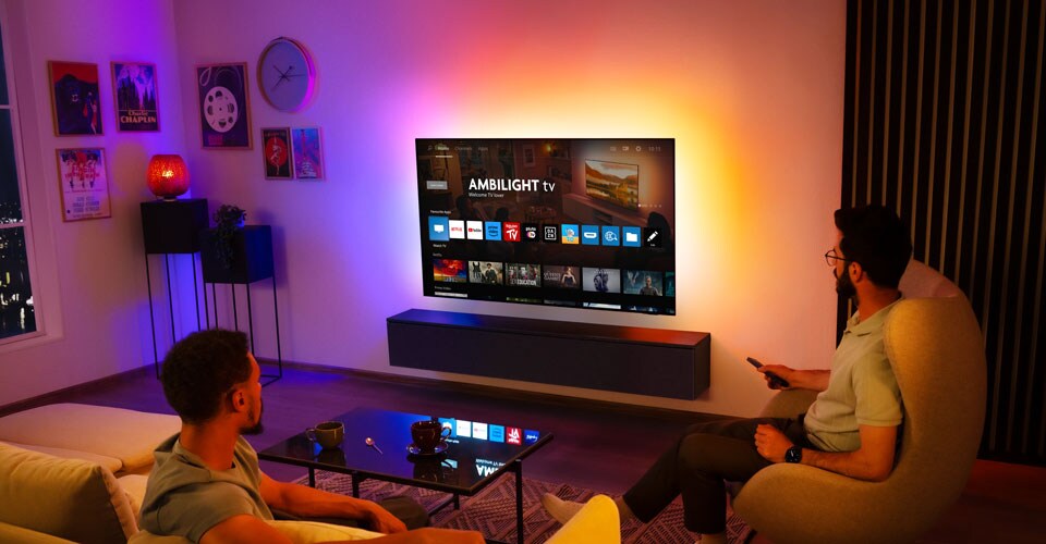 Divi vīrieši skatās pie sienas piestiprinātu Ambilight televizoru viesistabā