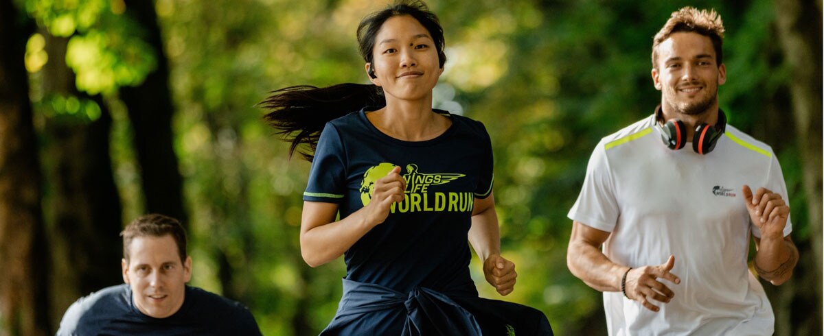 Trīs skrējiena “Wings for Life World Run” dalībnieki priecīgi skrien; ausīs tiem ir Philips sporta austiņas.
